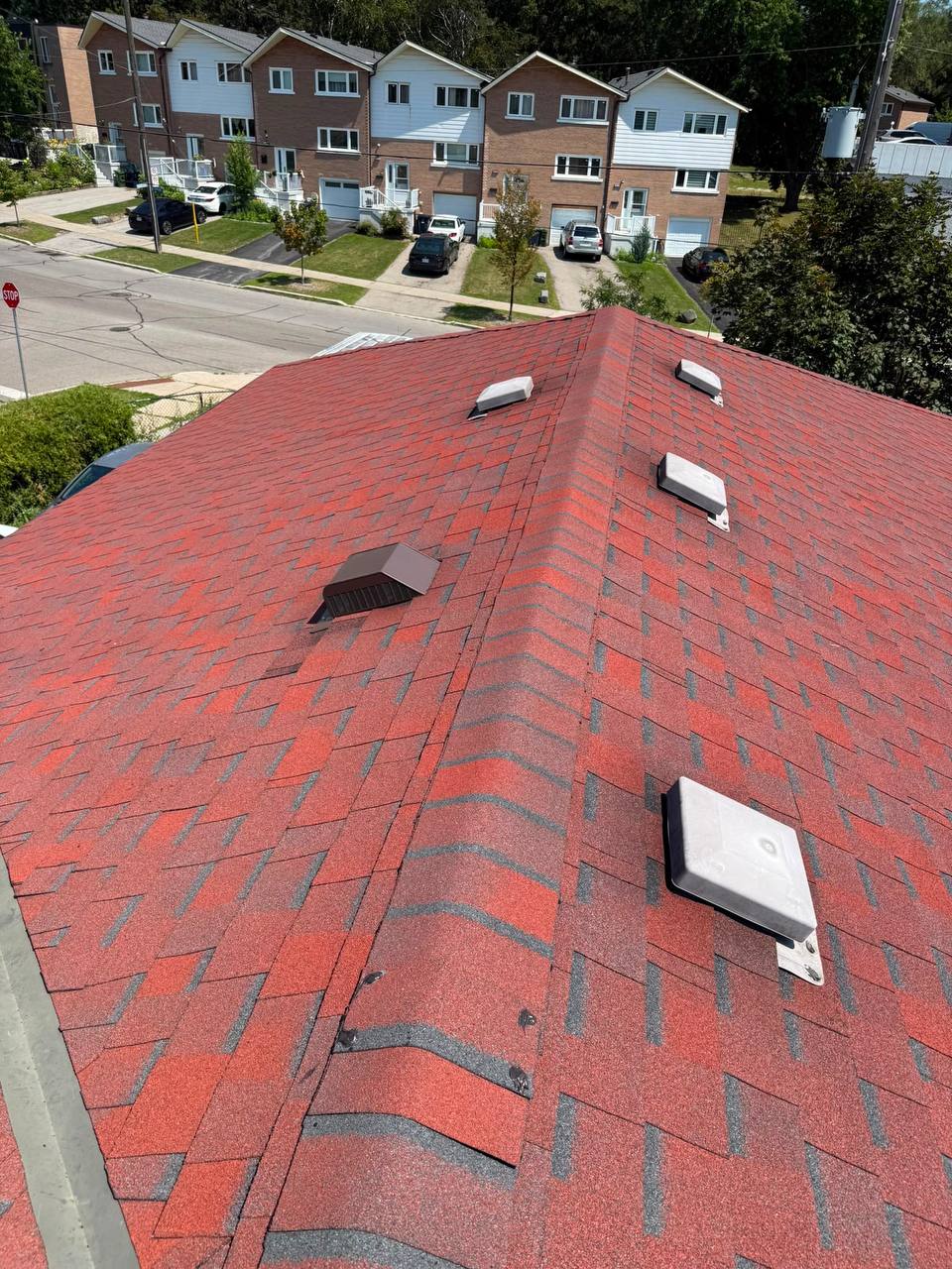 Red asphalt shingle roof with a brown roof vent and surrounding shingles after repair