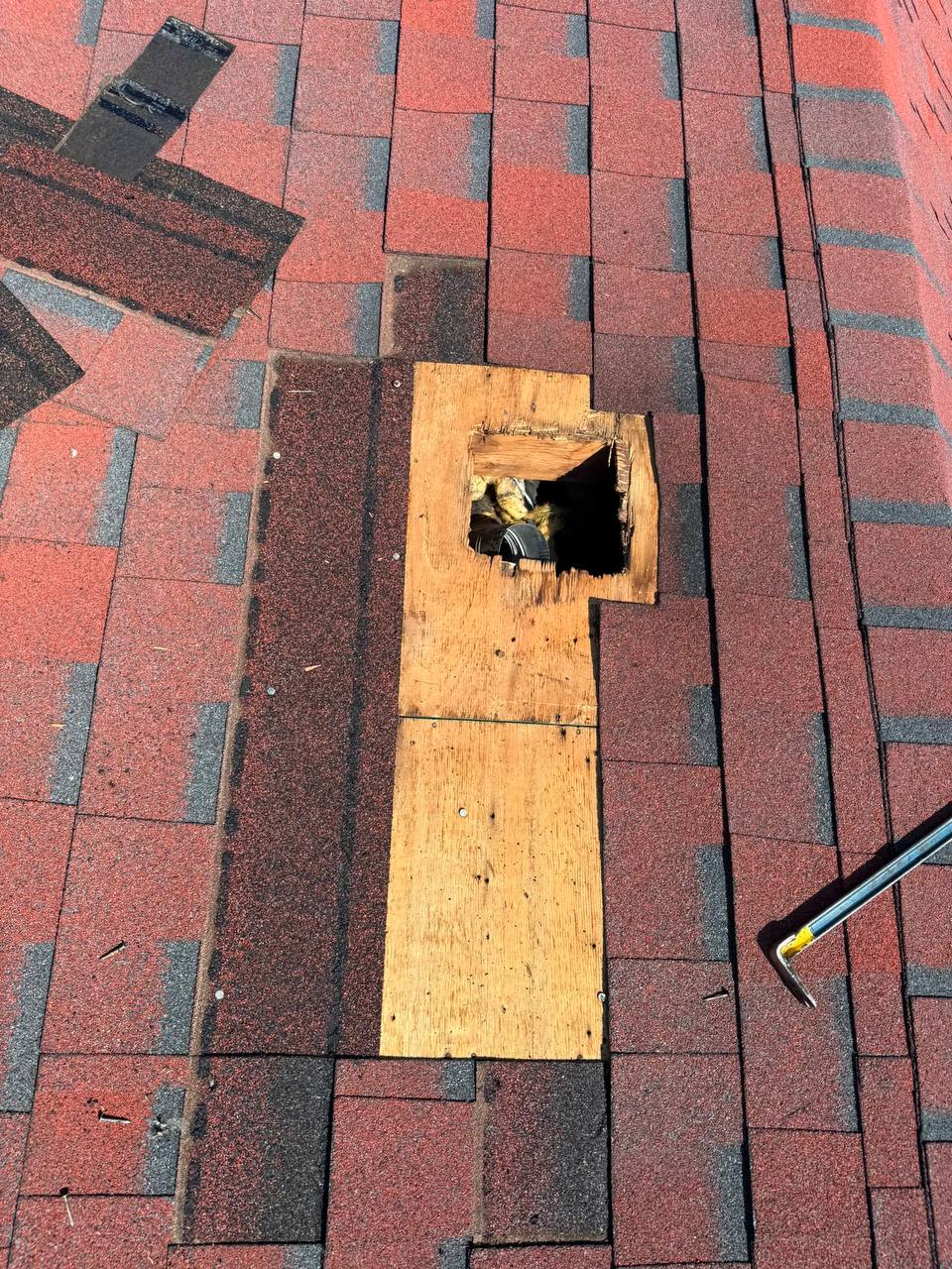 Exposed wood roof decking with an opening surrounded by red asphalt shingles