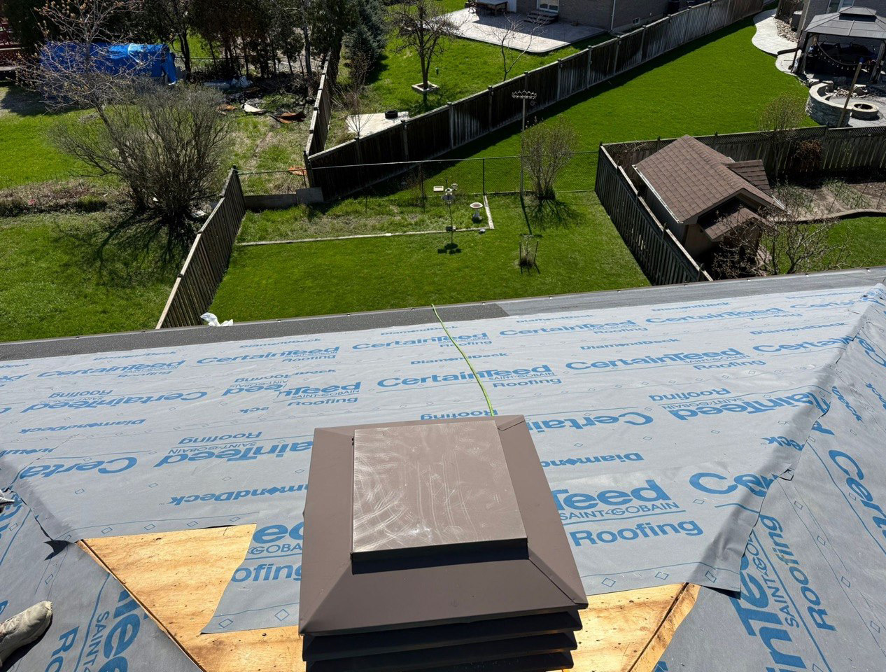 Brown roof vent surrounded by synthetic underlayment and exposed plywood decking