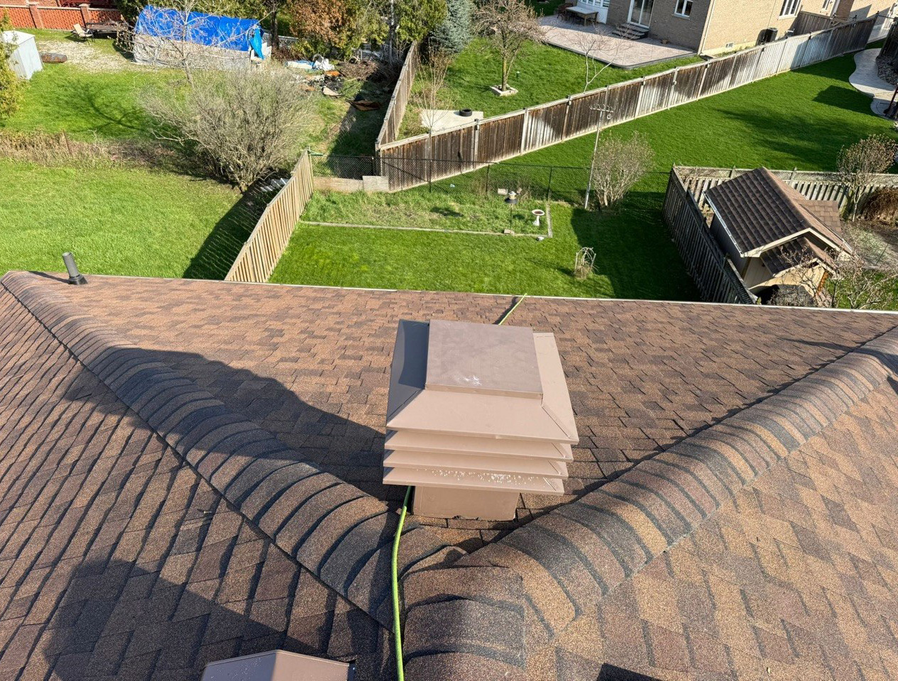 Brown roof vent surrounded by asphalt shingles and hip cap shingles
